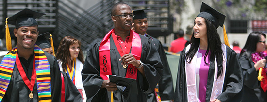 Three students walking in cap and gown